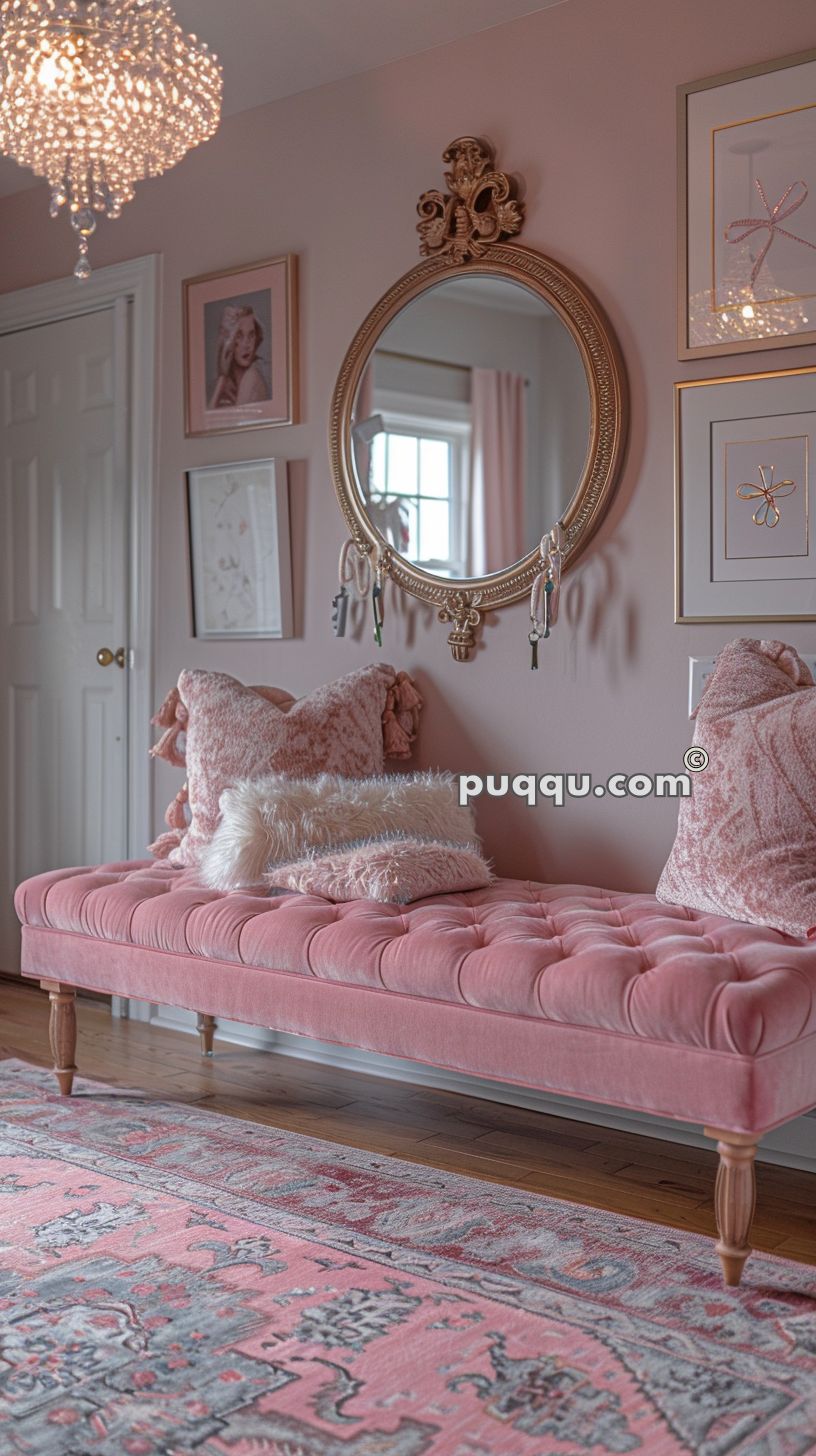 Elegant pink-themed room with a tufted pink bench, coordinated pillows, an ornate gold-framed oval mirror, framed artwork on the wall, a pink and gray patterned rug, and a crystal chandelier.