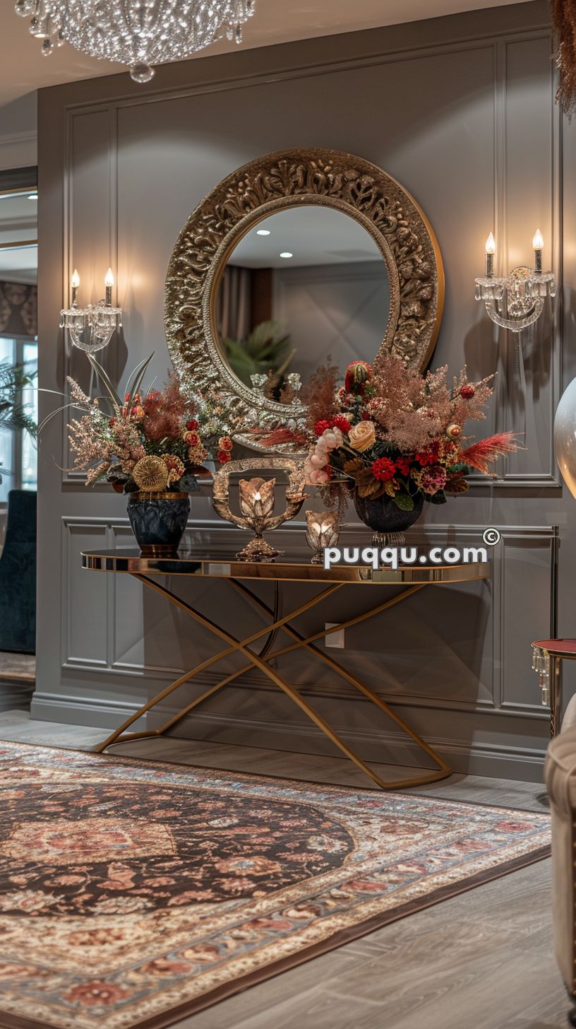 Elegant interior with a chandelier, ornate circular mirror, wall sconces, floral arrangements on a gold console table, and a patterned area rug.