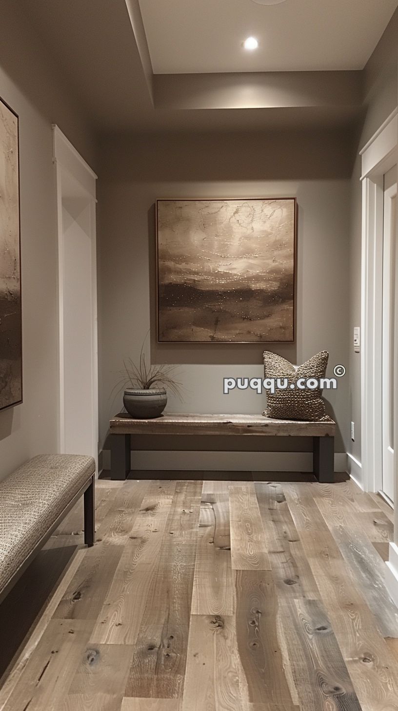 A hallway with a wooden bench against the wall, decorated with a potted plant and a textured cushion. Above the bench hangs a large abstract painting. The space features wooden flooring and neutral-toned walls.