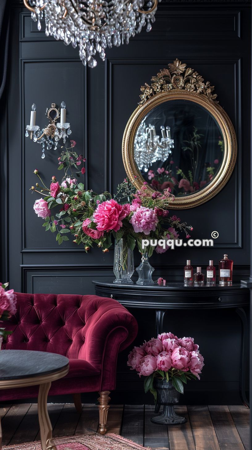 Elegant room with dark walls, ornate mirror, chandelier, red velvet sofa, floral arrangements, and perfume bottles on a black table.