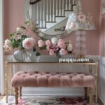 Elegant entryway with a pink tufted bench, floral rug, glass table adorned with vases of flowers, floral table lamp, and a round mirror reflecting a staircase.
