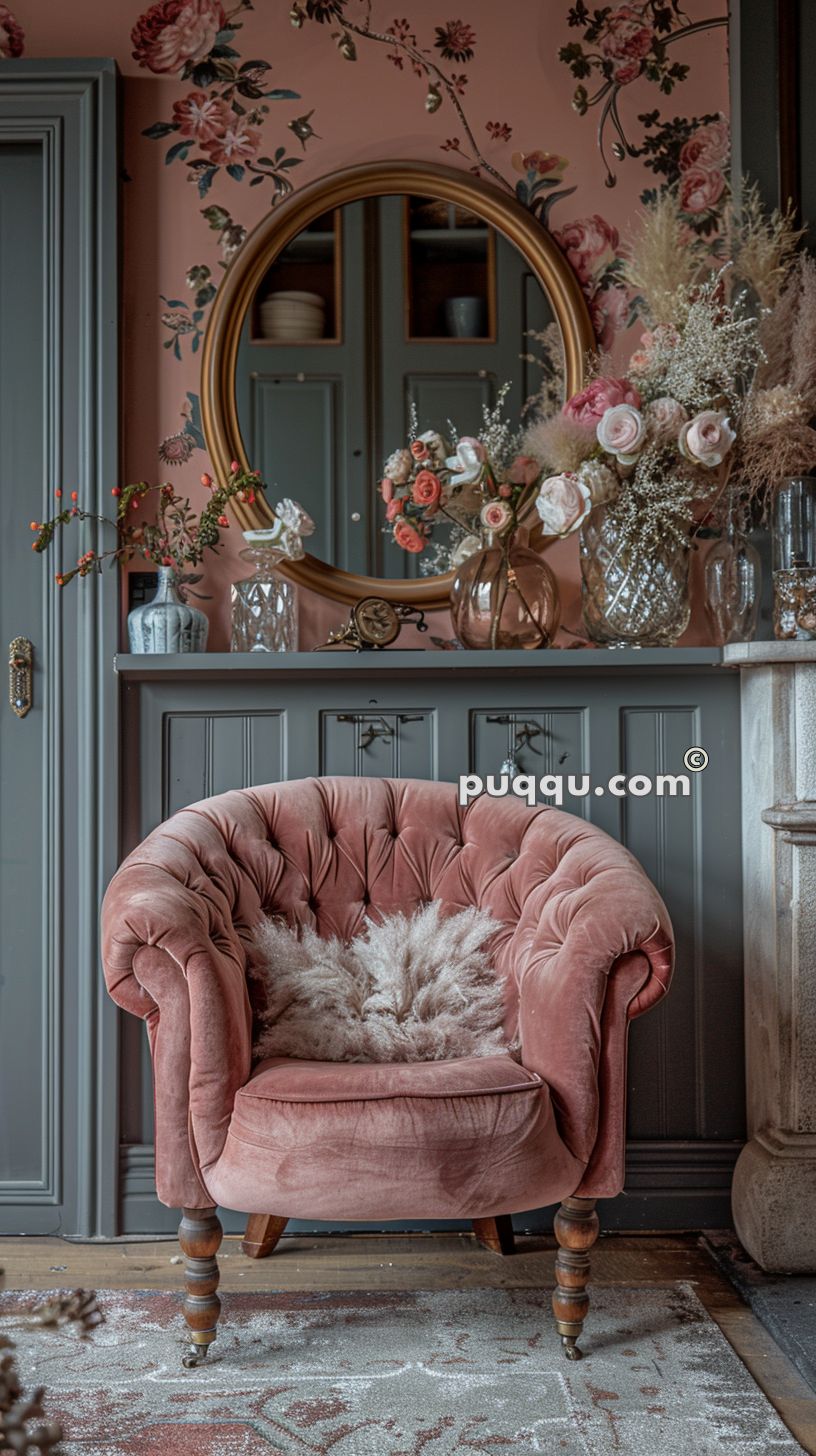 Vintage pink velvet armchair with a fluffy pillow against a floral wallpapered wall, featuring a round mirror and floral decorations.