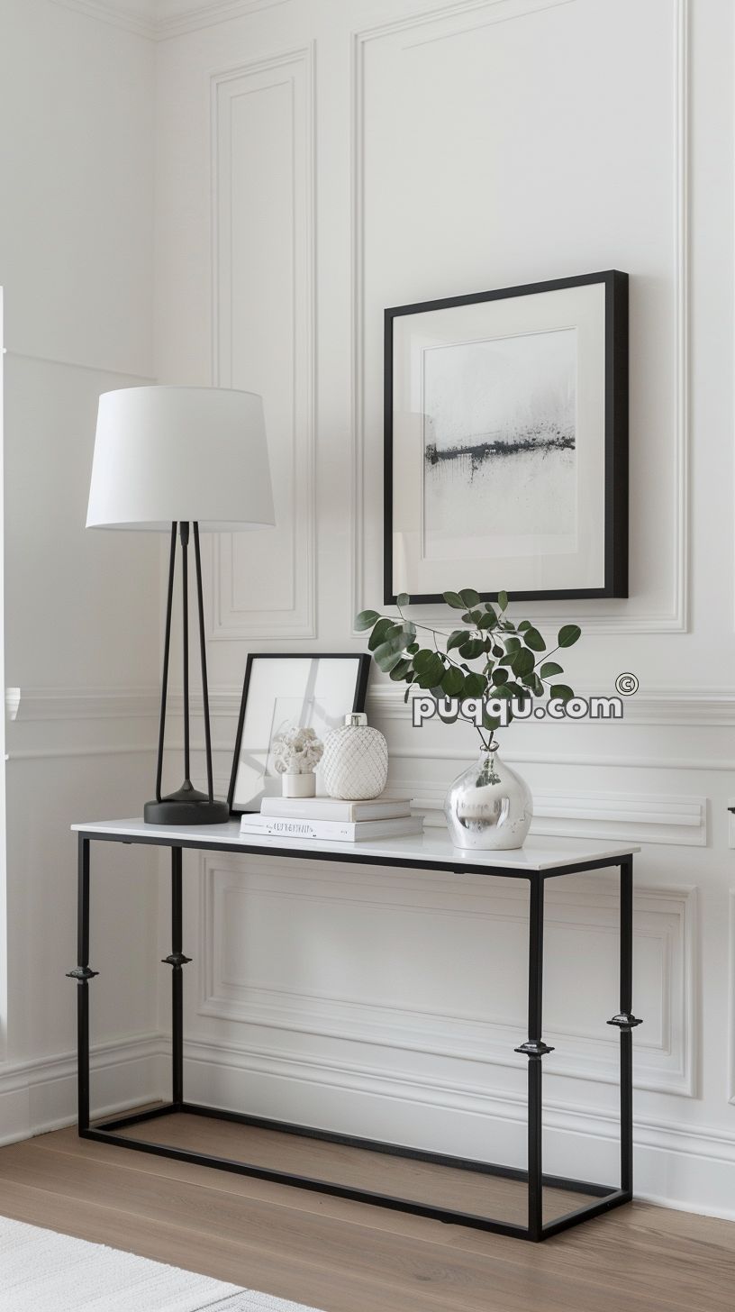 Modern decor with a black and white theme, featuring a black-framed abstract artwork, minimalist console table, table lamp, decorative vases, framed picture, and a small plant.