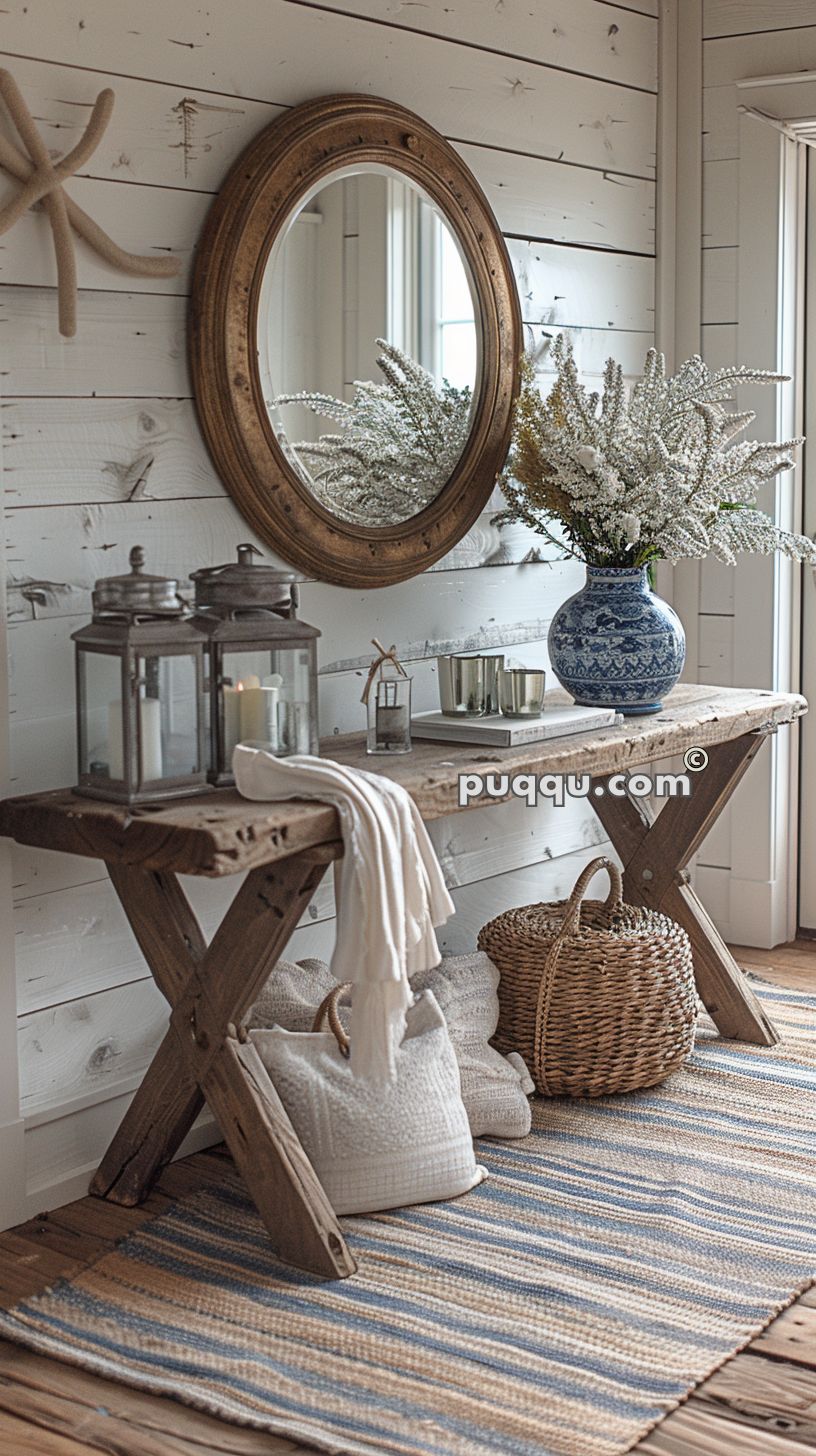 Rustic entryway with a wooden console table, round mirror, lanterns, blue and white vase with flowers, woven basket, throw blanket, and striped rug.