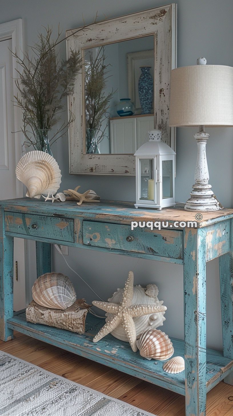 Rustic blue console table with various seashell decorations, a white lantern, a lamp, a mirror, and plants.