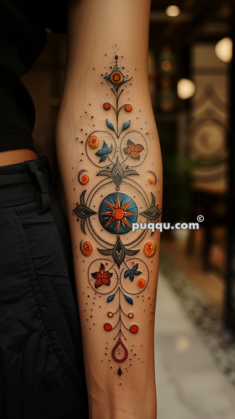 Detailed geometric and floral tattoo with blue, orange, and red accents on a person's forearm.