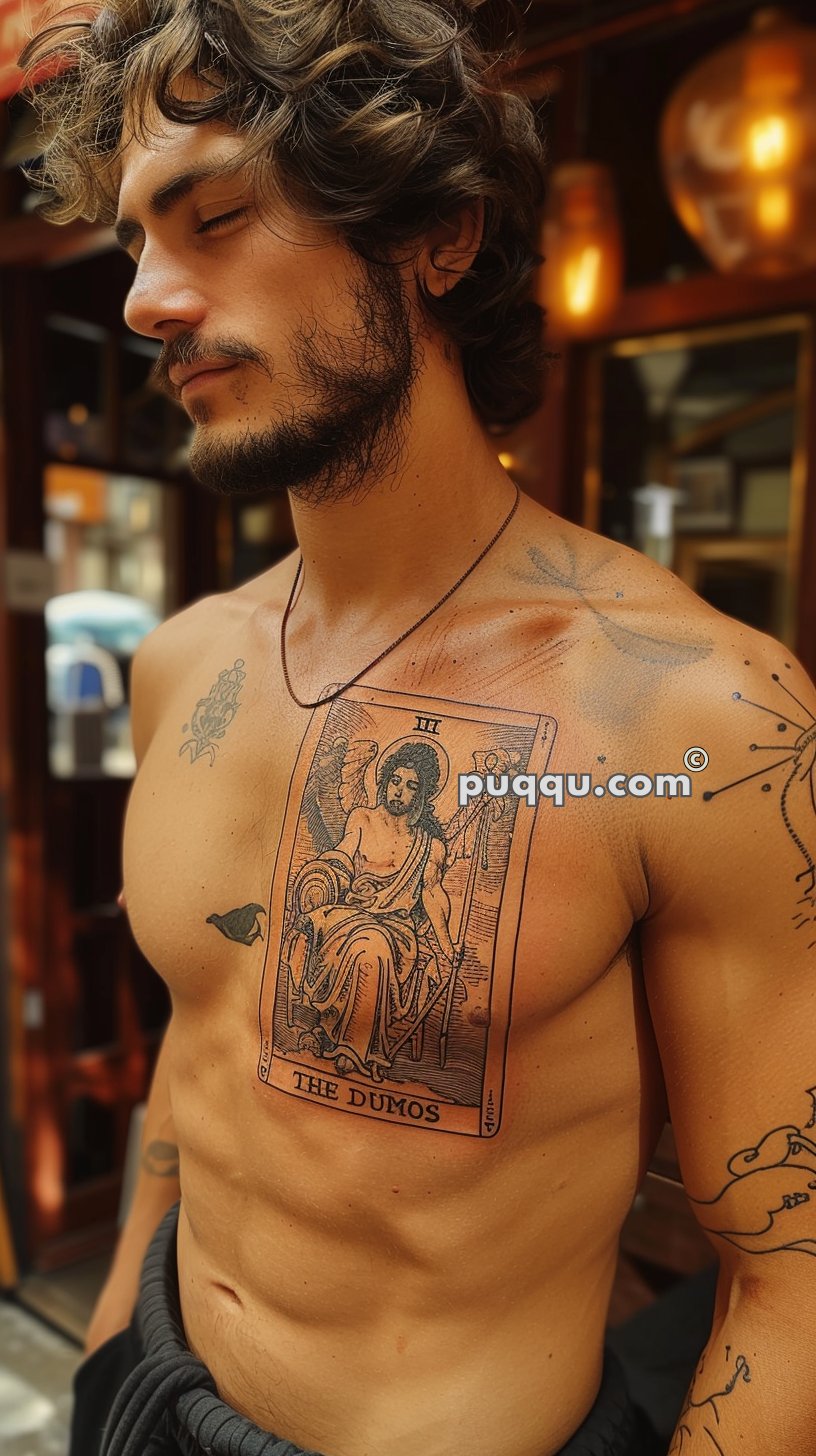 Man with curly hair and a beard, showcasing an intricate tattoo on his chest depicting an angelic figure with the words "THE DUMOS."