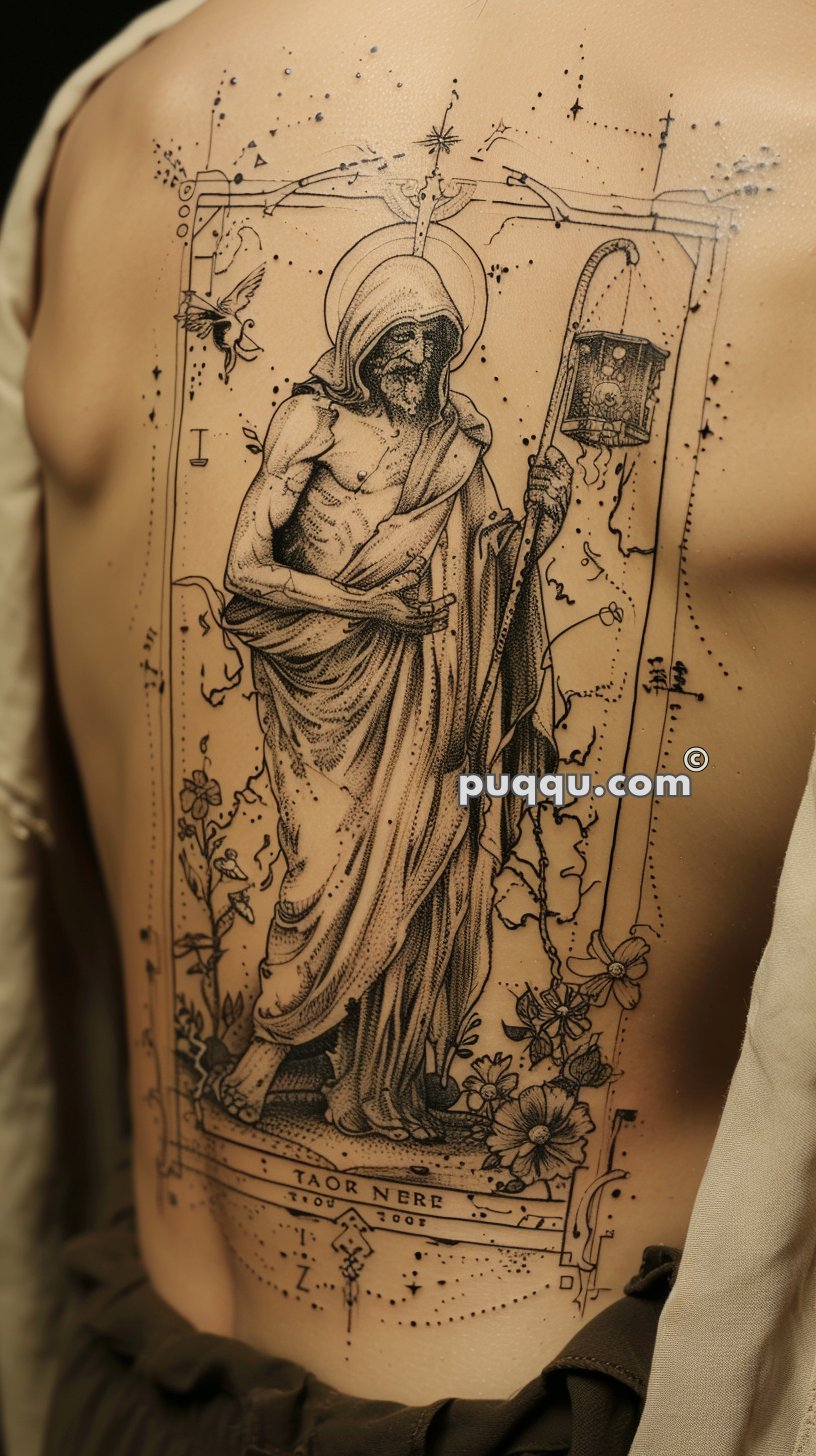 Tattoo of a robed, hooded figure holding a lantern, surrounded by floral elements and bordered by ornate designs on someone's back.