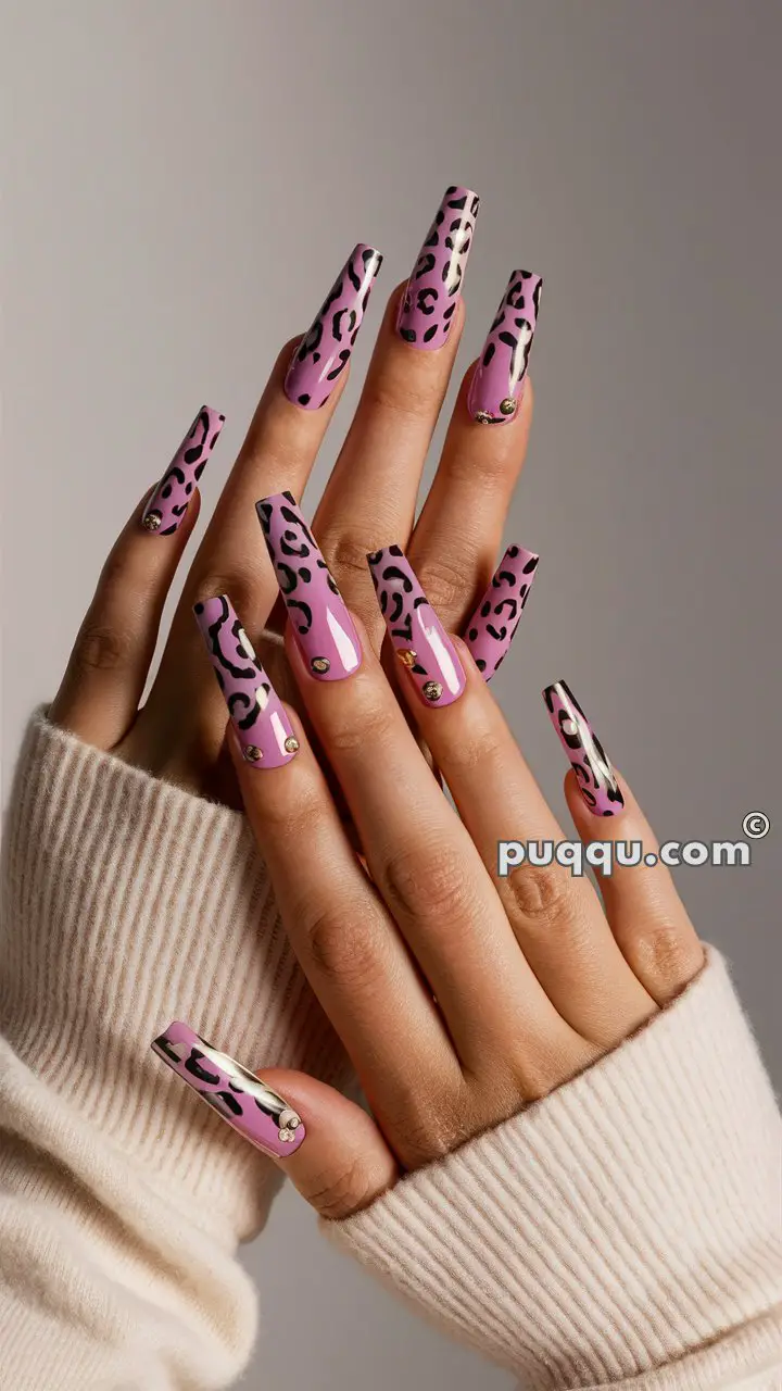 Hands with long, pink, leopard-print nails adorned with small gold studs, wearing a cream-colored sweater.