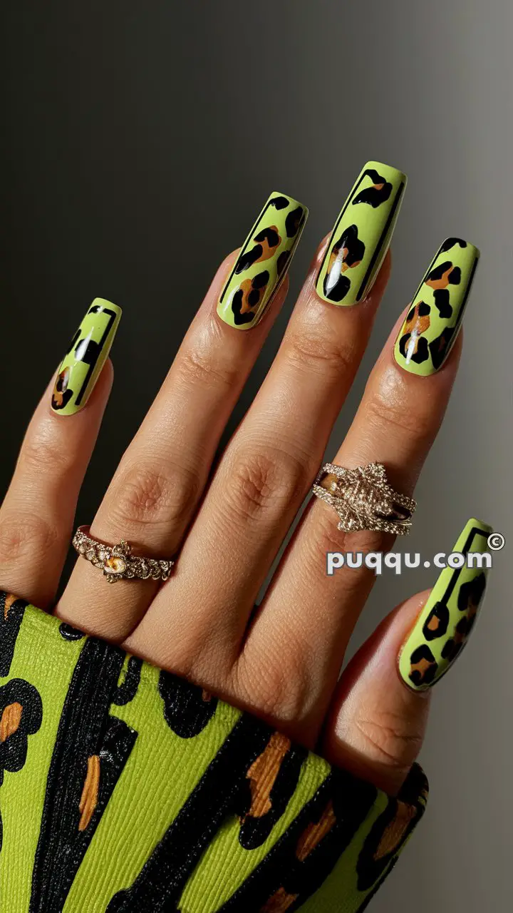 Hand with long, neon green and black leopard print nails, wearing multiple rings, against a dark background.