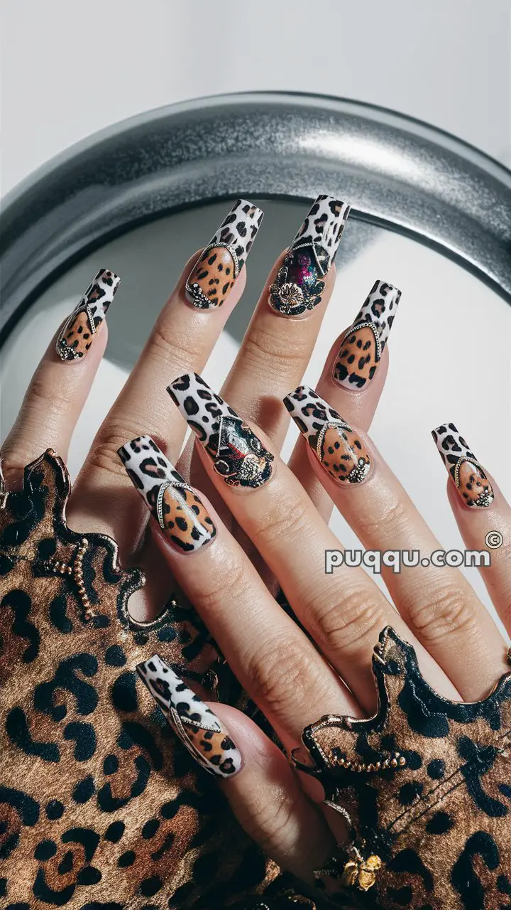 Hands with long stiletto-shaped nails featuring leopard print and black and white spotted designs, adorned with gemstone accents. The hands are dressed in leopard print fabric gloves.