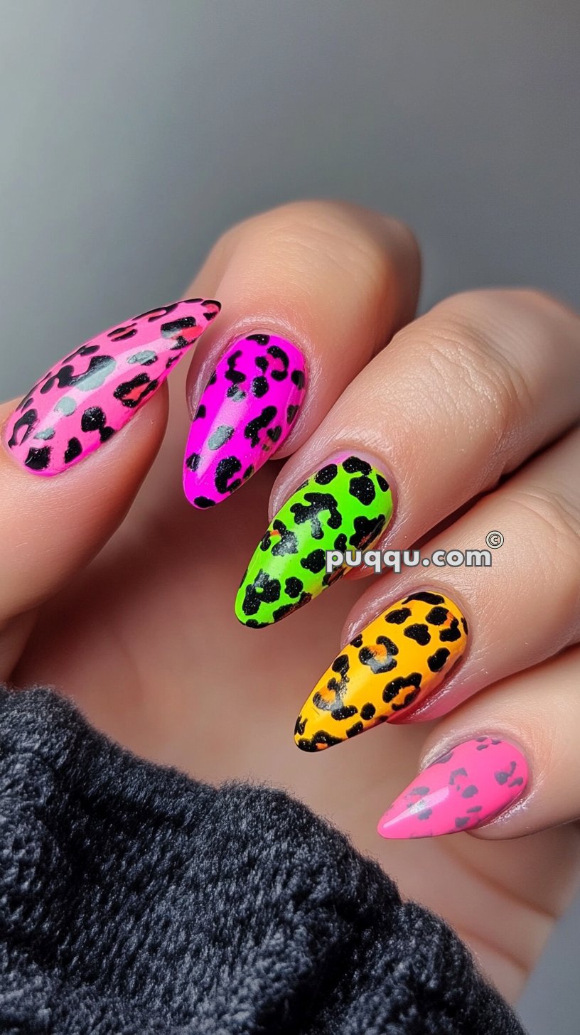 Close-up of a hand with stiletto-shaped nails featuring colorful neon leopard print designs.