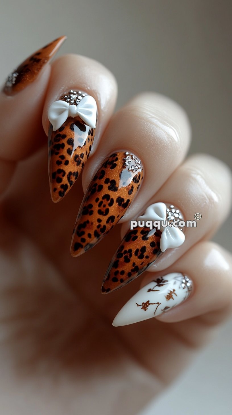 Close-up of a hand with long, pointed nails featuring leopard print design, embellished with 3D white bows and rhinestones.