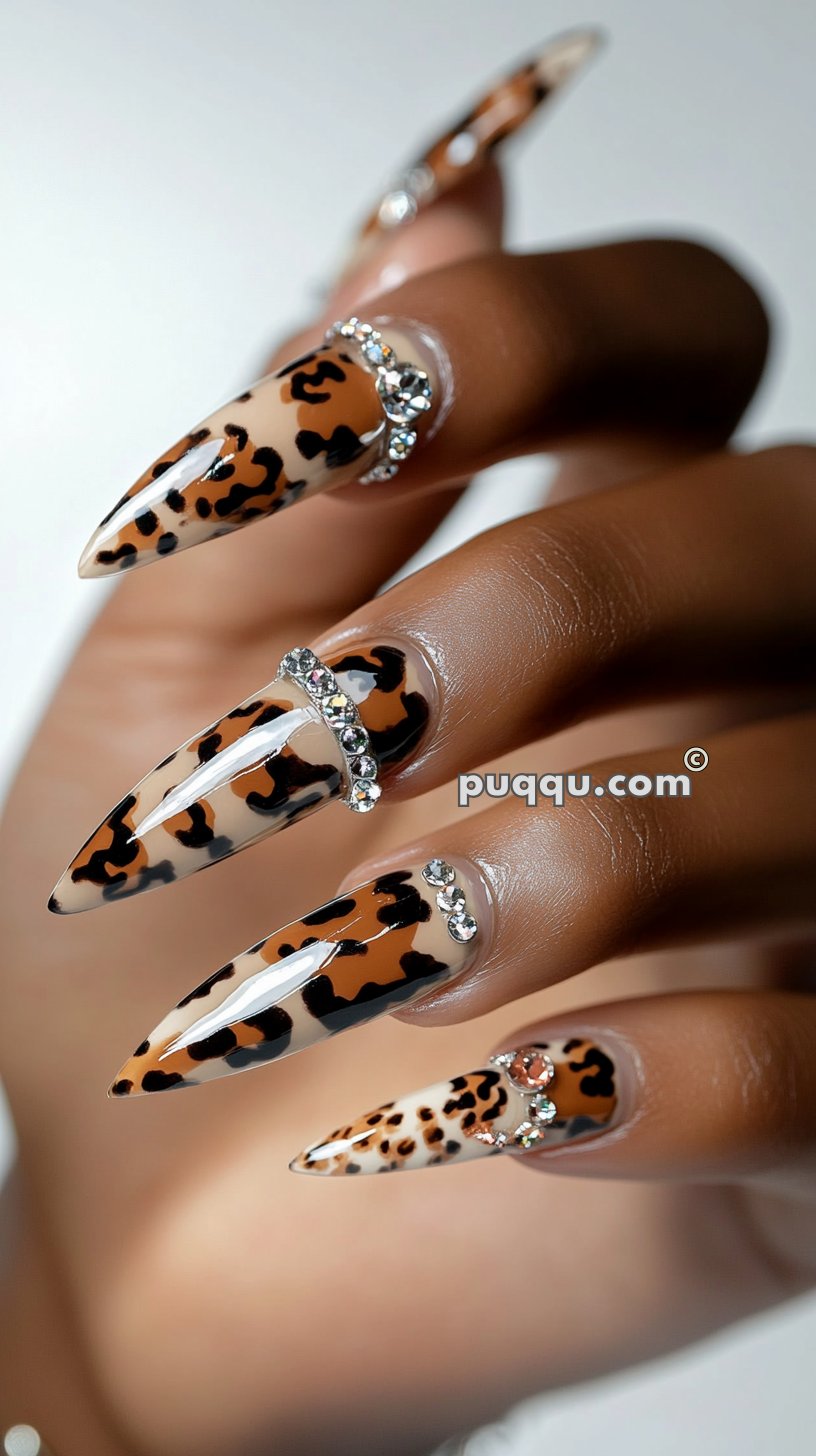 Hand with long, pointed nails featuring leopard print design and decorated with diamond-like gems.