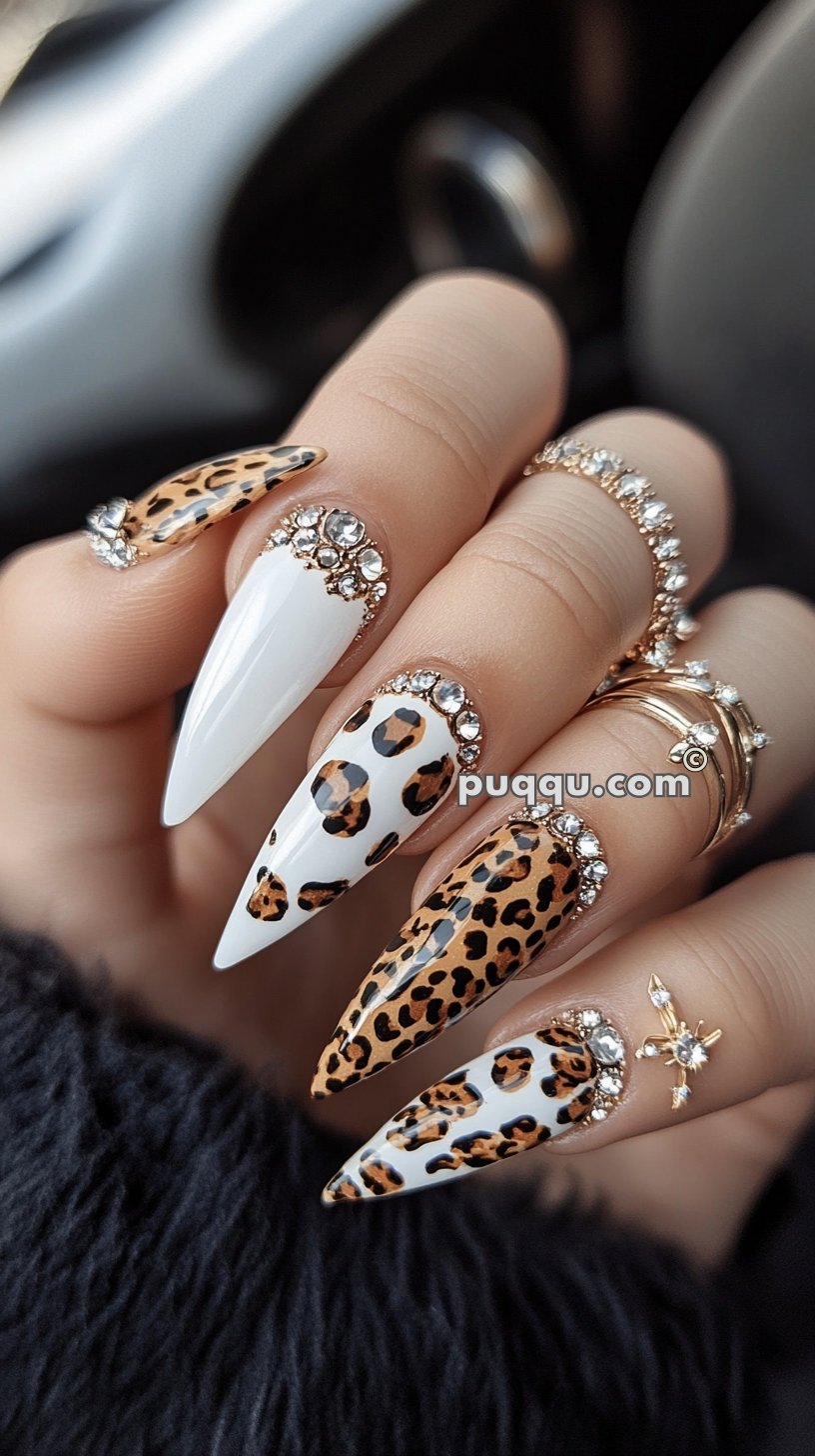 Long pointed nails with mixed designs including leopard print and solid white, embellished with rhinestones.