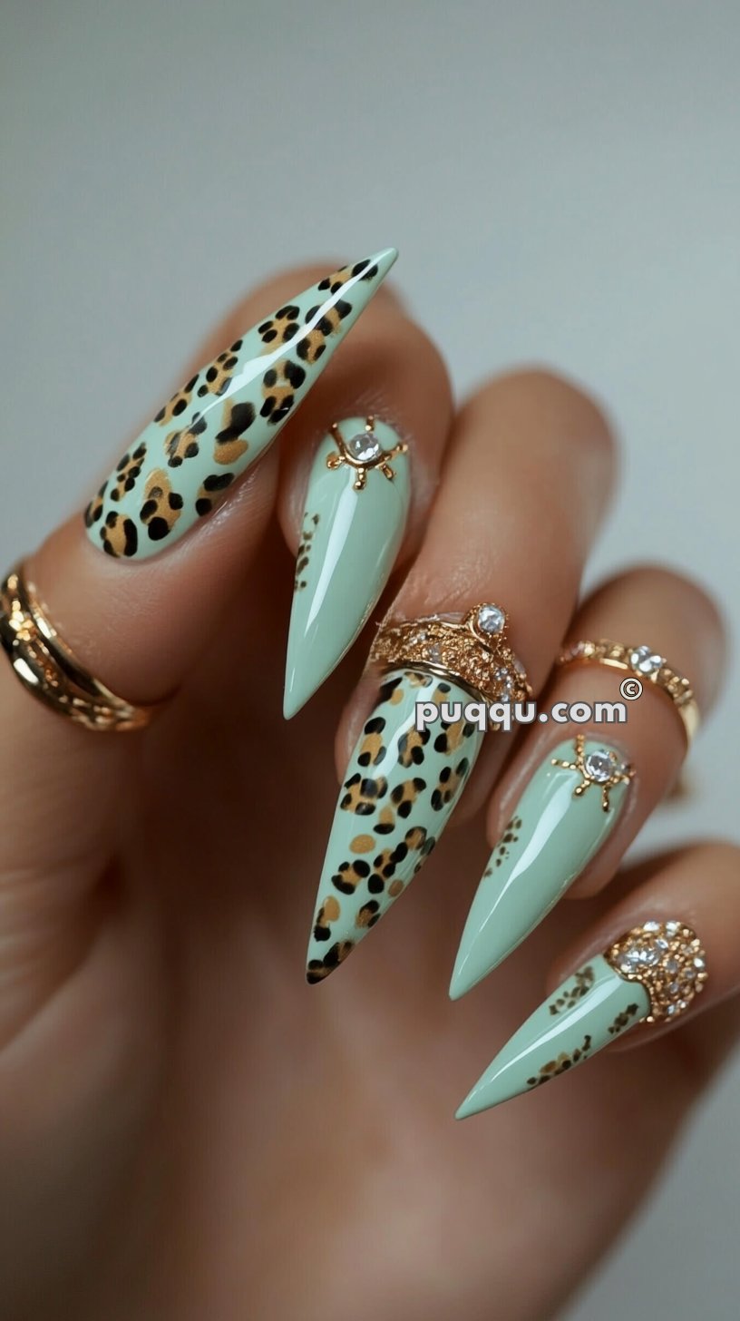 Long stiletto nails painted in light green with black and brown leopard print accents, adorned with gold and rhinestone embellishments.