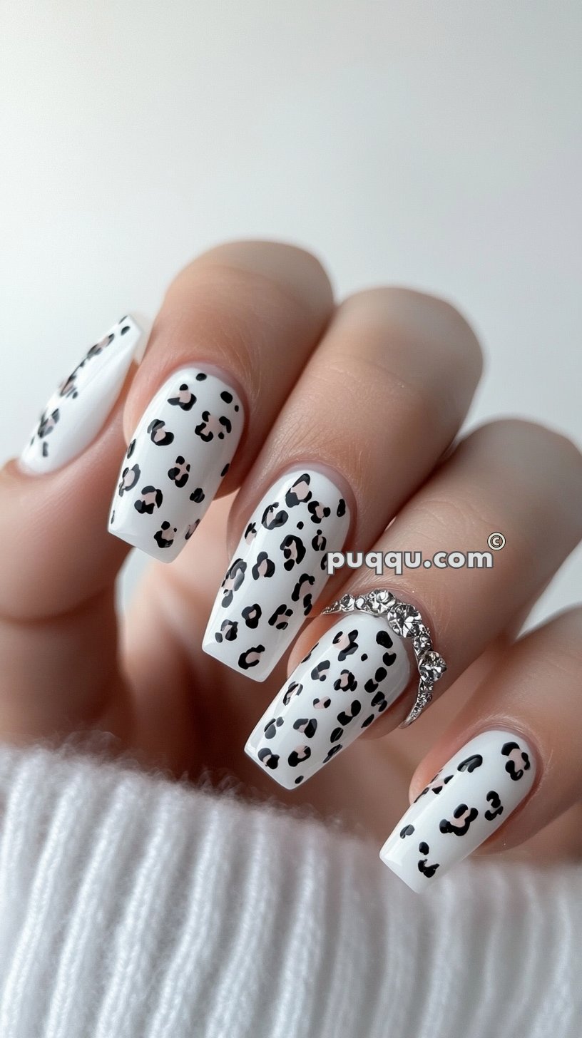 Close-up of white nails with black leopard print design, one hand wearing a jeweled ring on the ring finger.