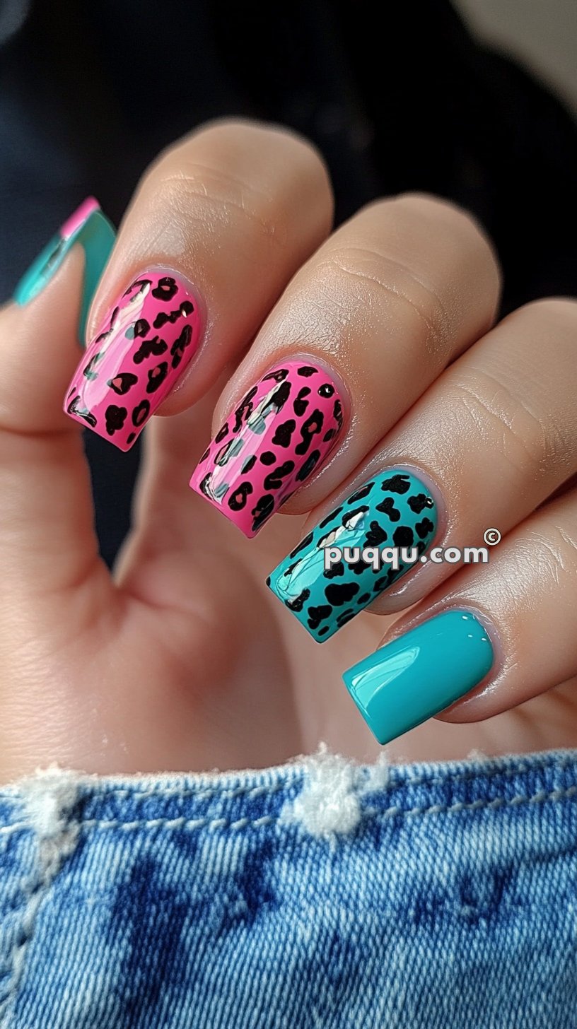 Close-up of a hand with colorful leopard print nail art. The nails have two pink and two teal leopard print designs, alongside one solid teal nail.