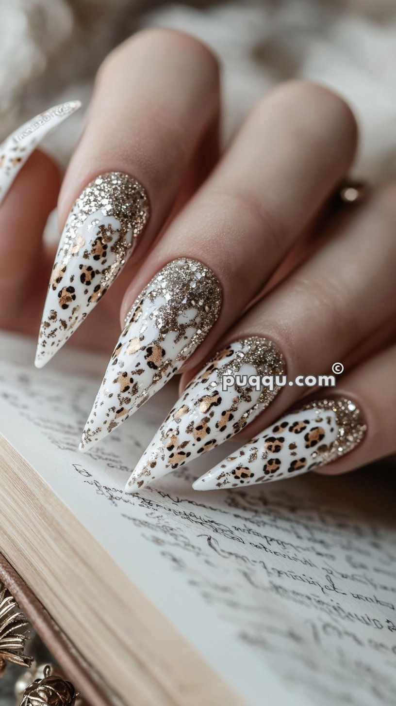 Close-up of a hand with long, stiletto-shaped nails featuring a glittery leopard print design over white polish, resting on an open book.