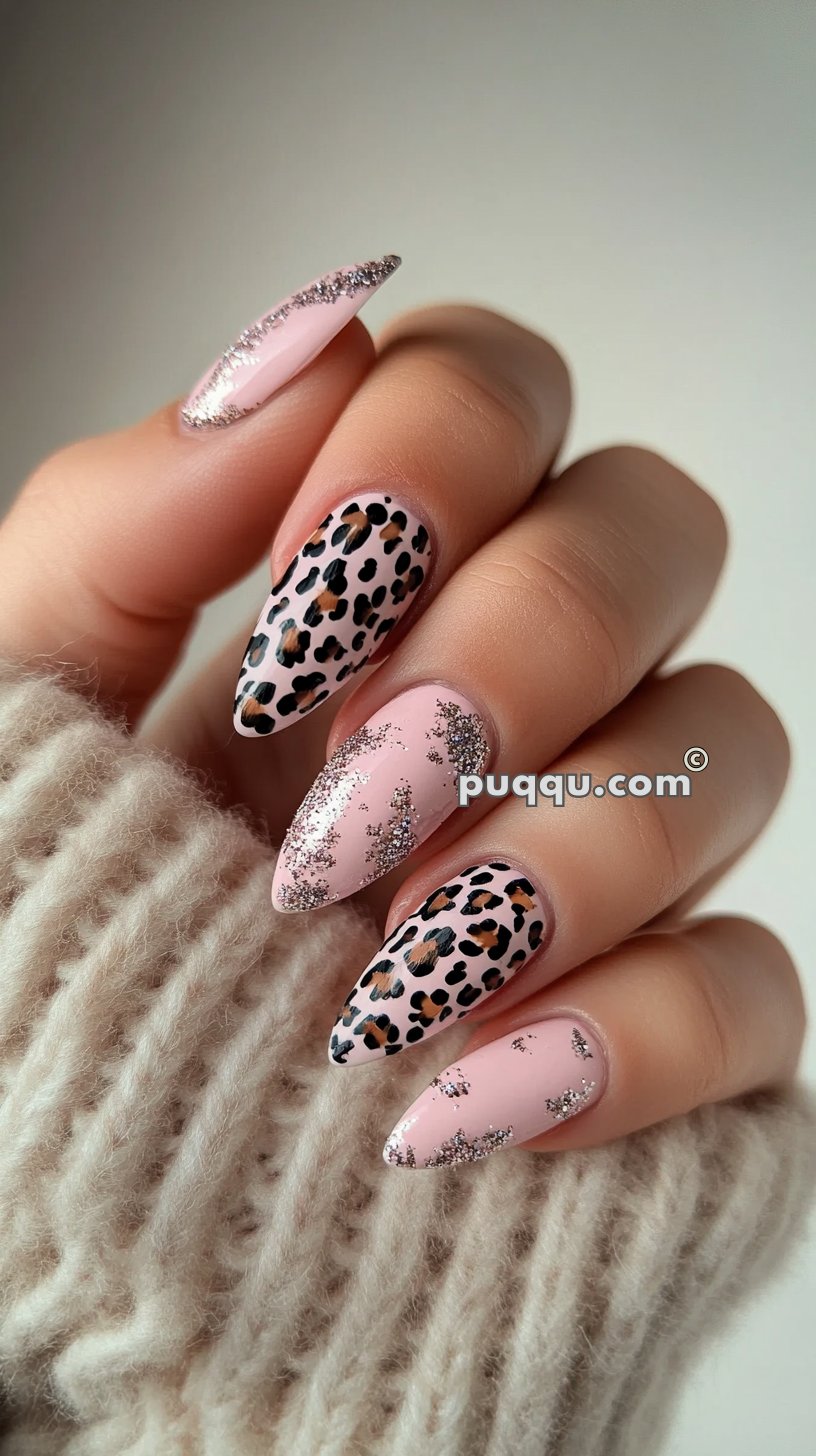 Almond-shaped nails with a light pink base featuring leopard spots and silver glitter accents, held by a hand in a fuzzy cream sweater.