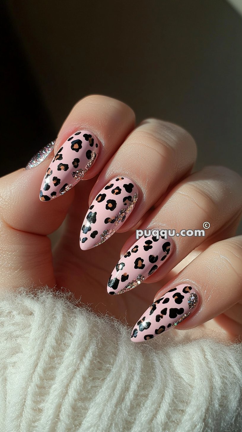 Long, almond-shaped nails with pink polish featuring black leopard spots and glitter accents.