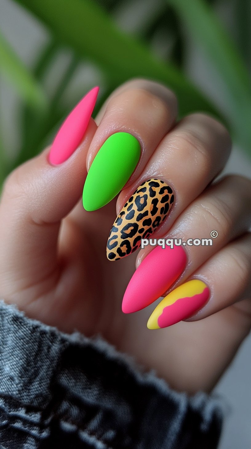 Hand with brightly colored, stiletto-shaped nails in neon pink, green, leopard print, and a yellow-pink gradient.