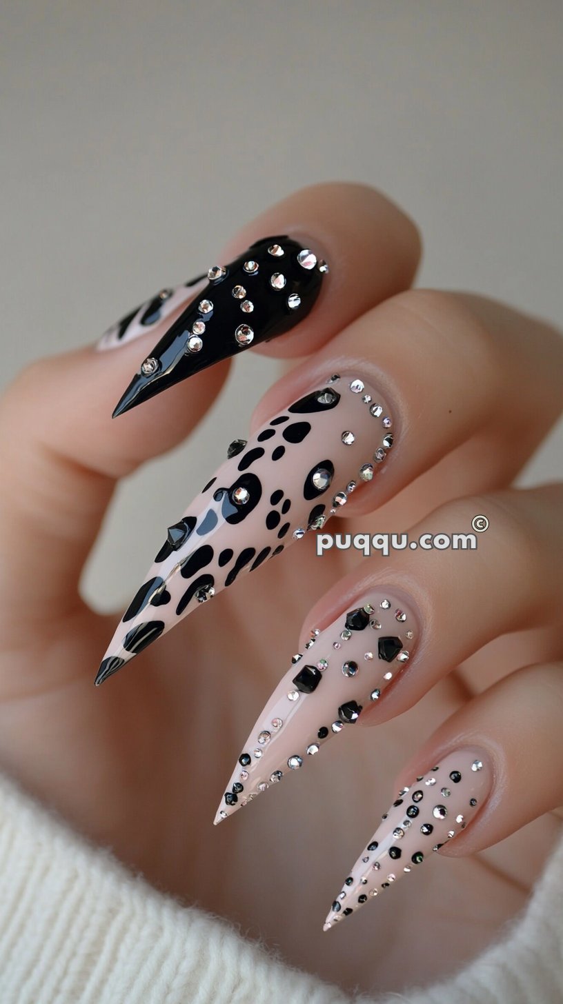 Long stiletto-shaped nails with a mix of nude and black designs, embellished with rhinestones and black polka dots.