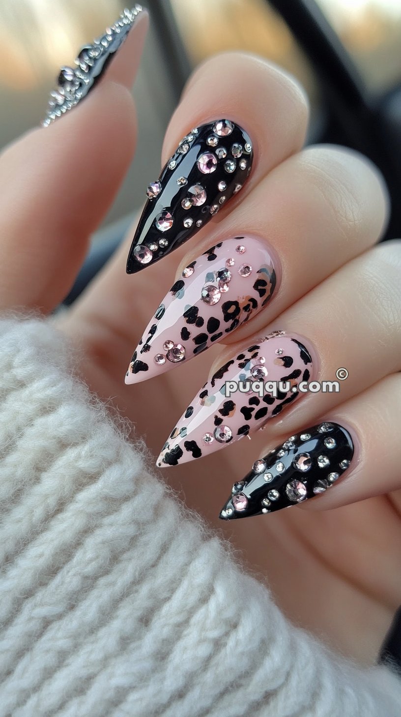 Close-up of stiletto-shaped nails decorated with black and pink polish, leopard print patterns, and pink rhinestones.