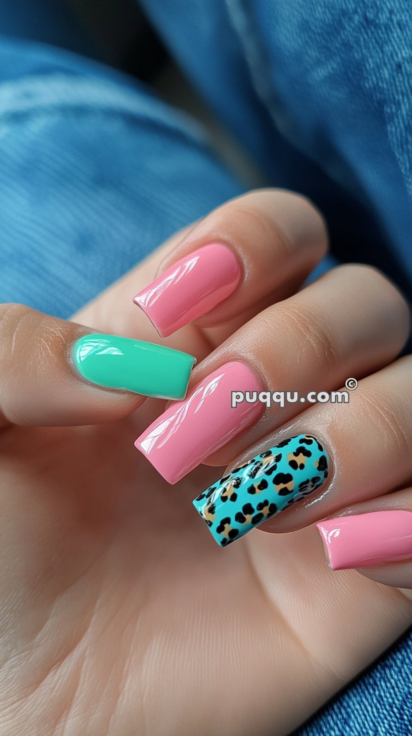 Hand with long nails painted in different colors: pink, teal, and teal with a leopard print design.