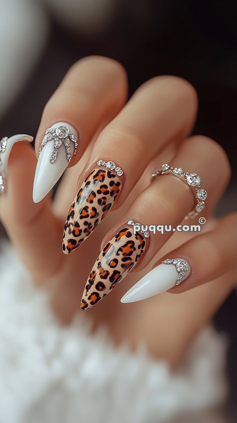 Close-up of manicured hands with long, sharp nails featuring white polish, leopard print, and rhinestone embellishments.