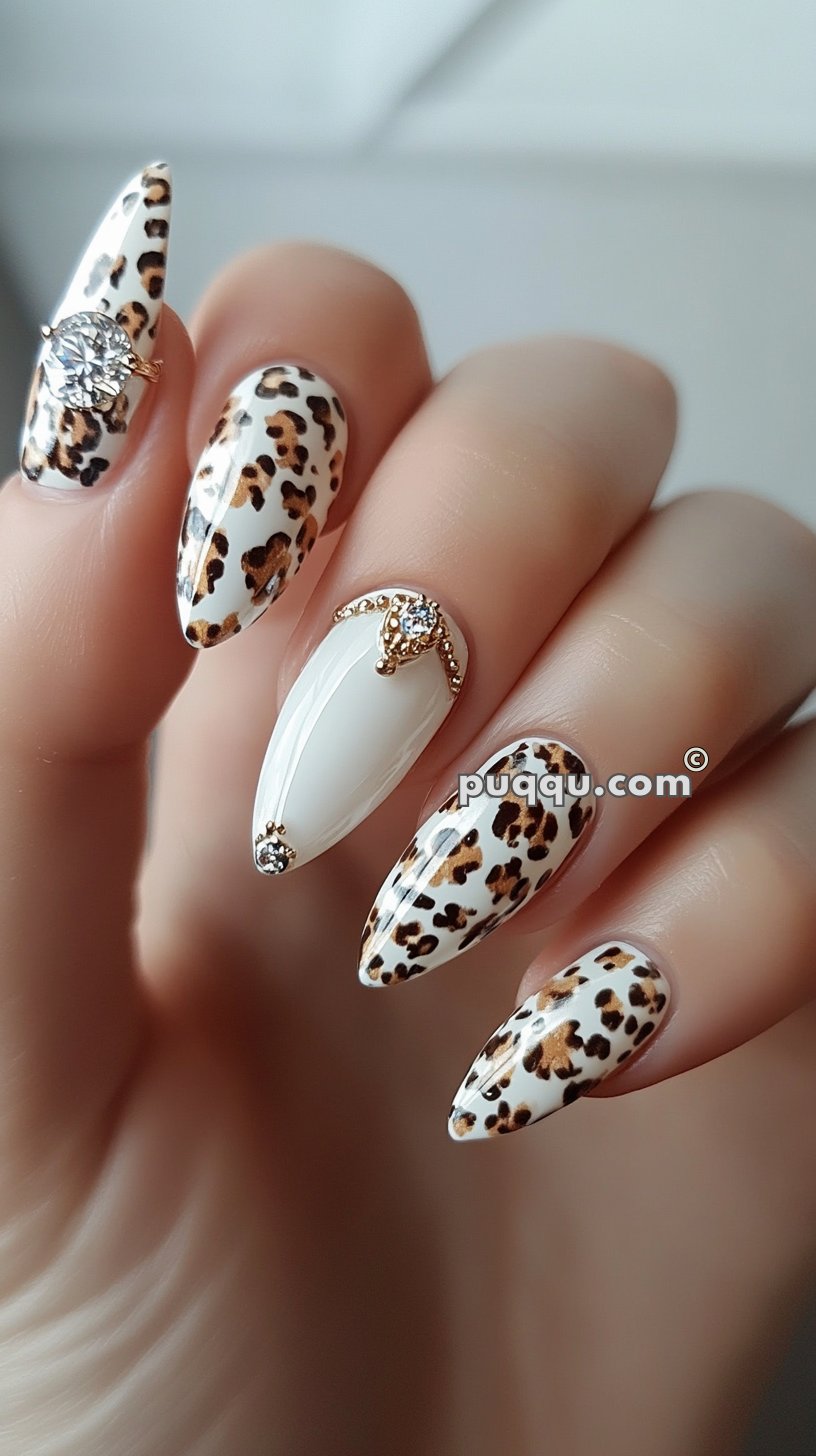 Close-up of a hand with long stiletto-shaped nails featuring a leopard print design, accented with rhinestones and gold embellishments.