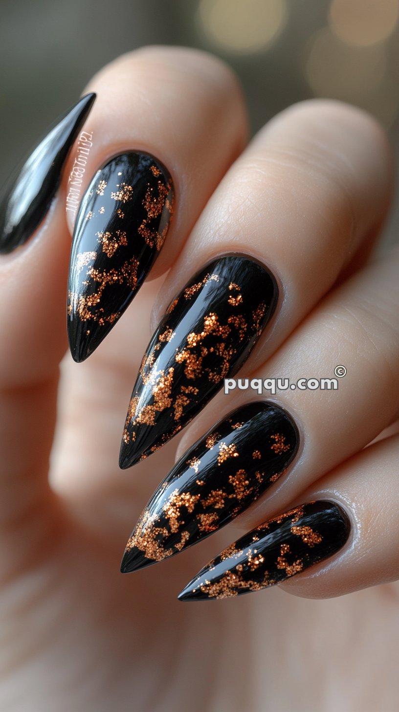 Long, pointed black nails with gold glitter accents.