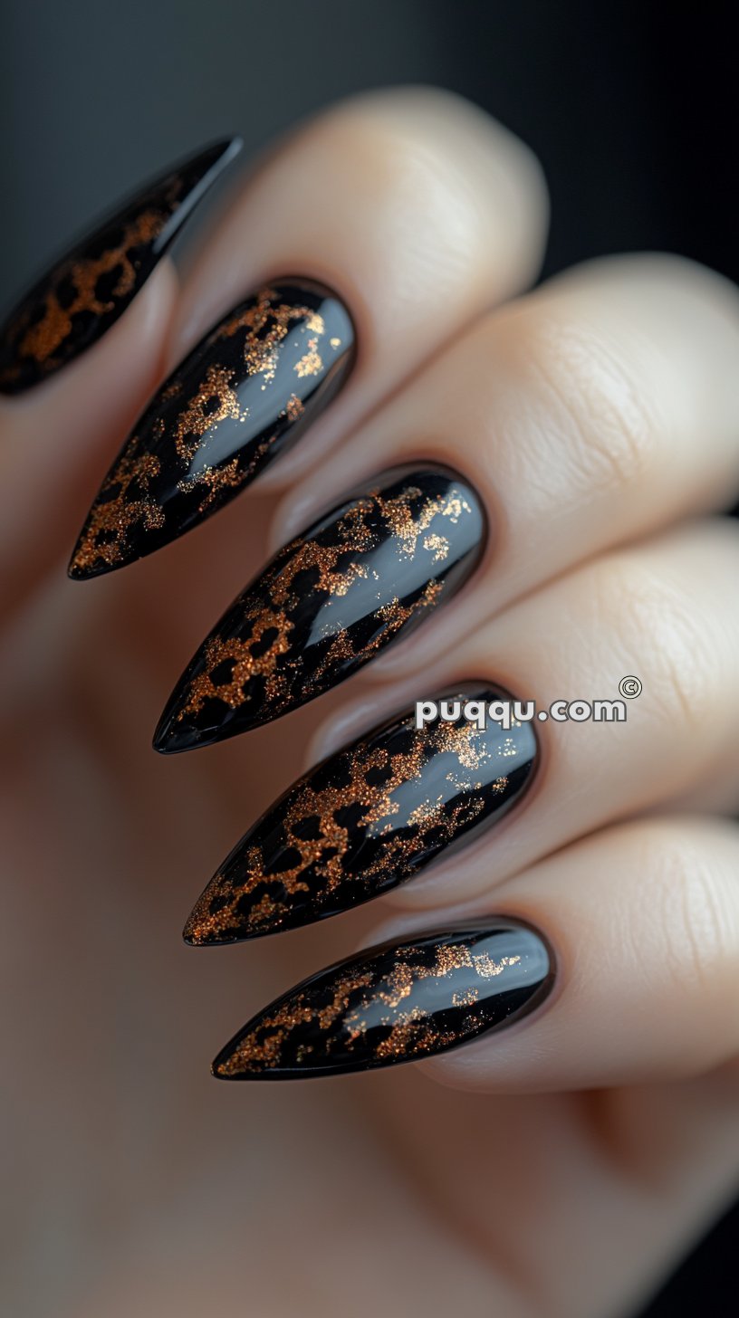 Close-up of a hand with long, stiletto-shaped nails painted with a shiny black base and adorned with copper glitter leopard print design.