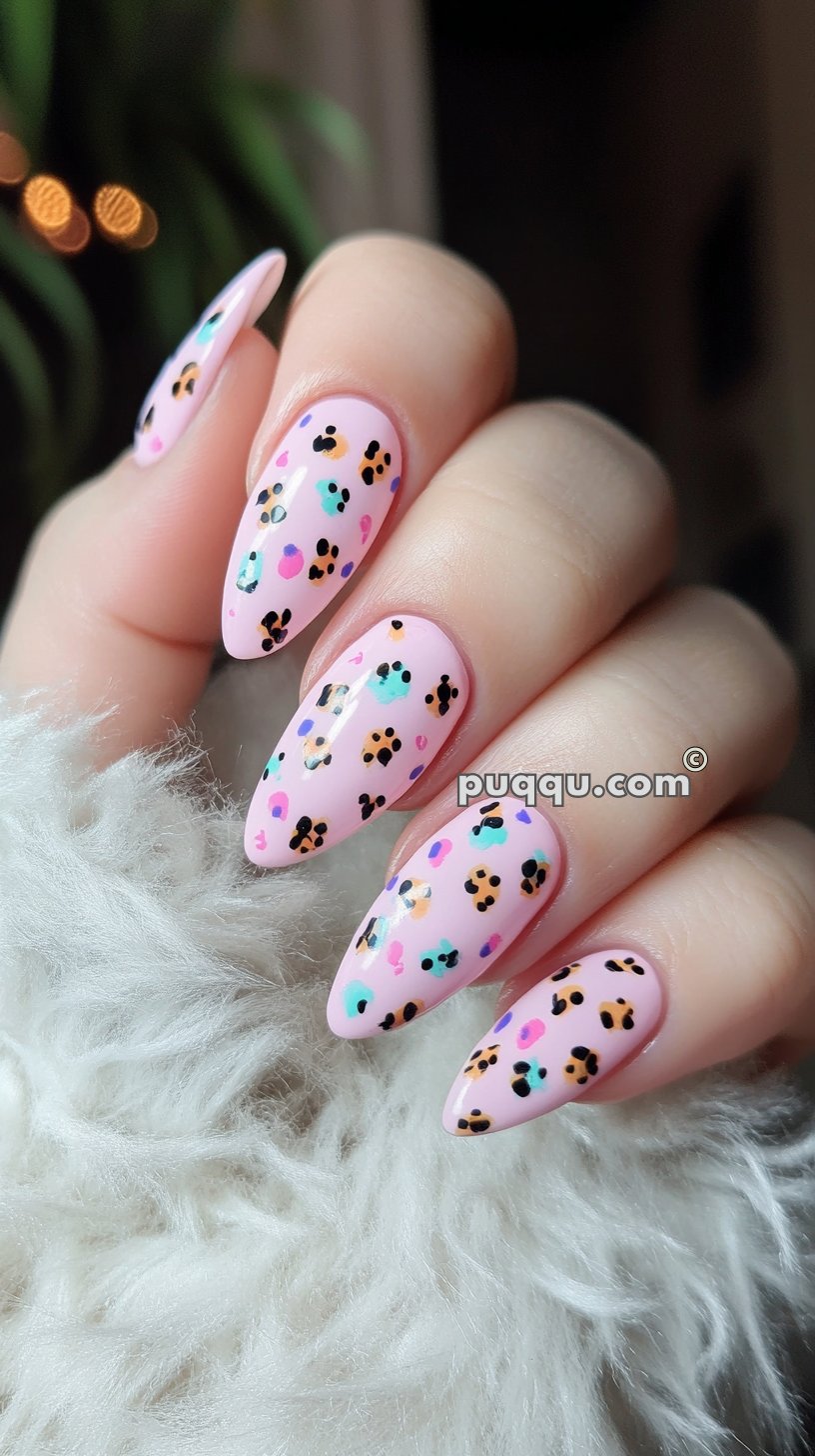 Close-up of a hand with long, almond-shaped nails featuring pastel pink polish with colorful leopard print accents.