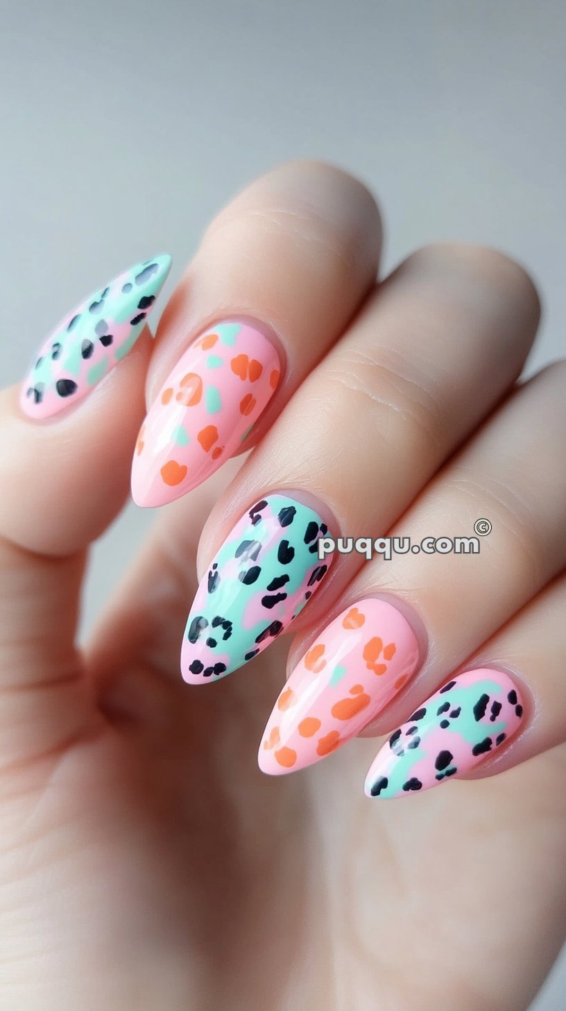 Hand with long, pointed nails featuring a colorful leopard print design in pink, mint green, black, and orange.