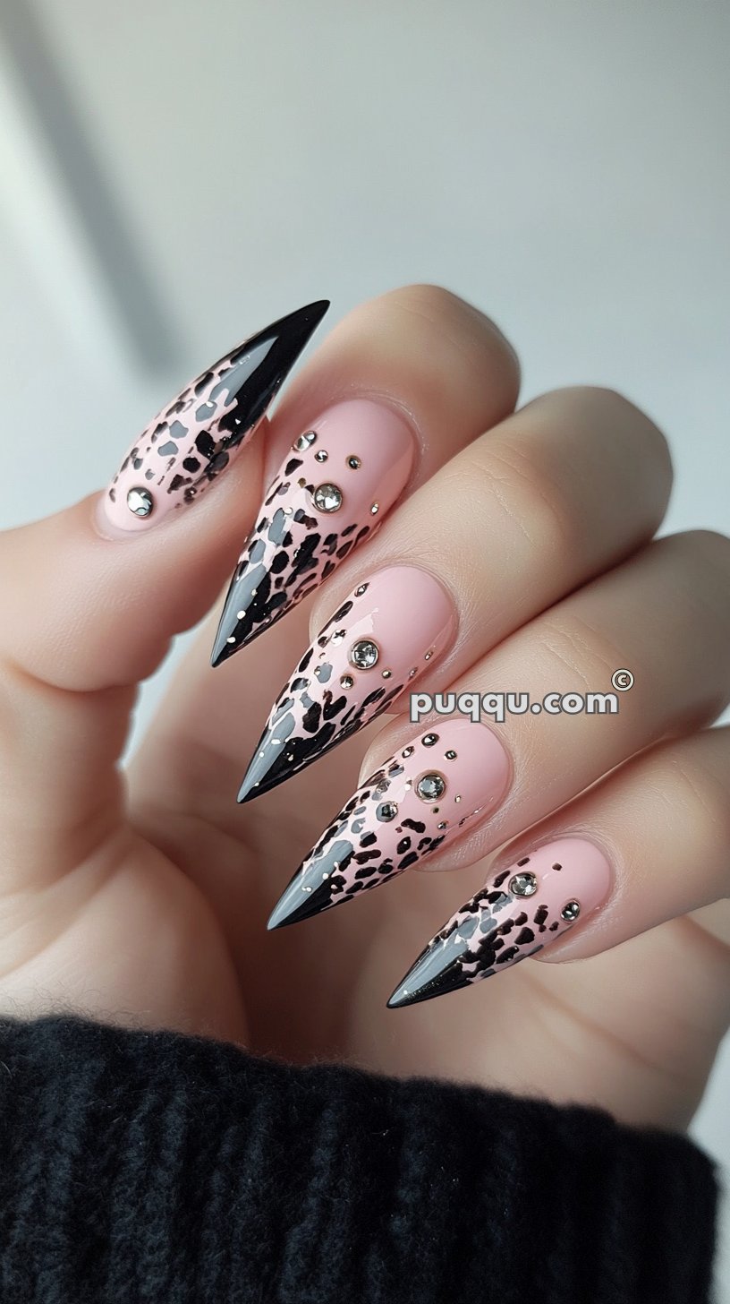 Long, pointed nails with a pink and black leopard print design, black tips, and rhinestone accents.