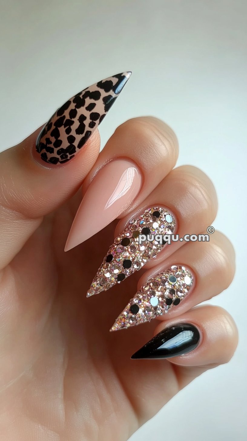 Close-up of a hand with stiletto-shaped nails decorated in various designs, including leopard print, nude polish, glitter with black dots, and solid black.