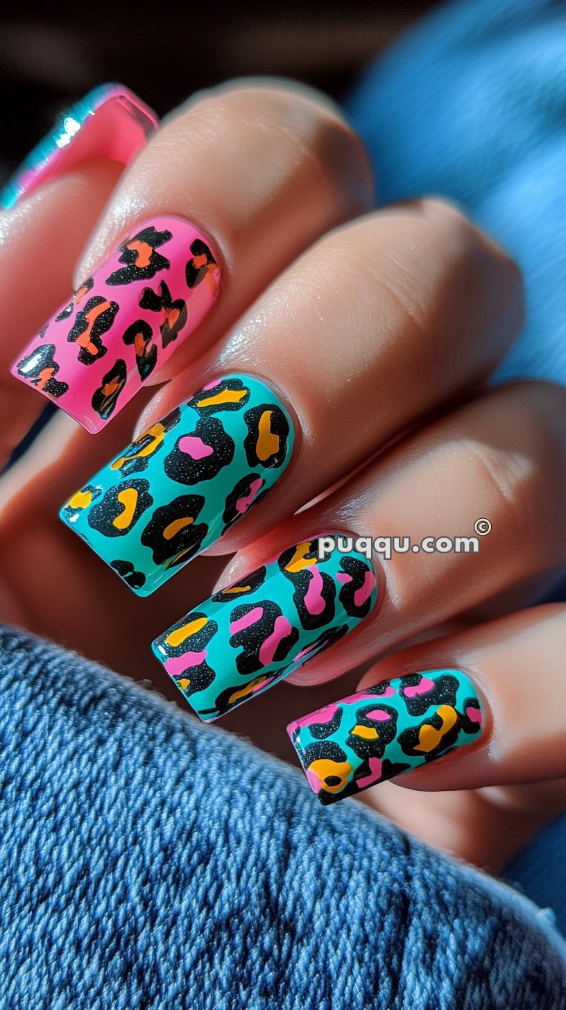 Colorful leopard print nail art on long square-shaped nails, featuring pink and teal backgrounds with yellow, black, and pink spots.