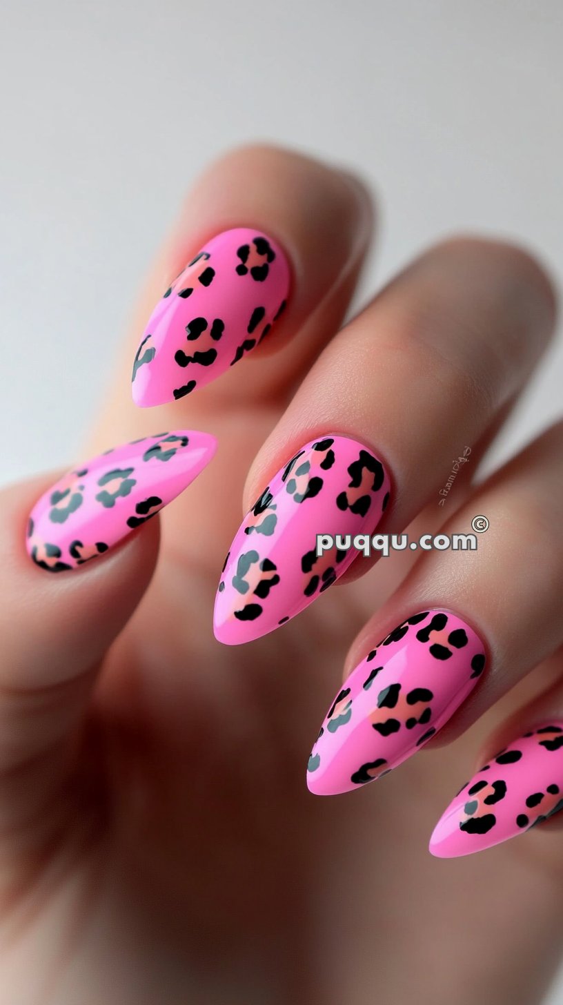 Close-up of manicured nails with a pointed shape, painted in bright pink with black leopard spots.