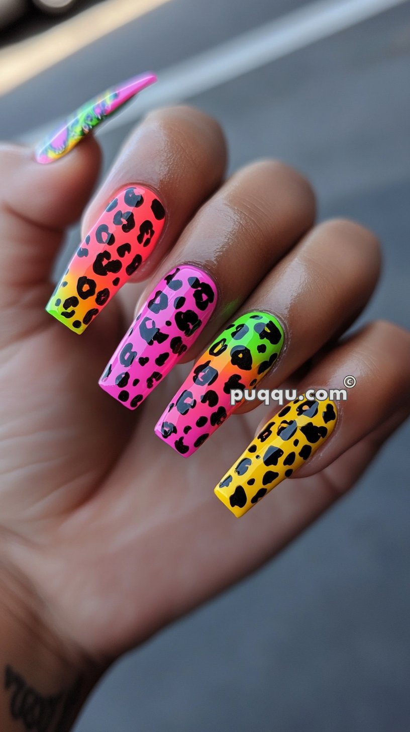 Hand with long, square-shaped nails featuring colorful, gradient leopard print designs in neon pink, green, and yellow.