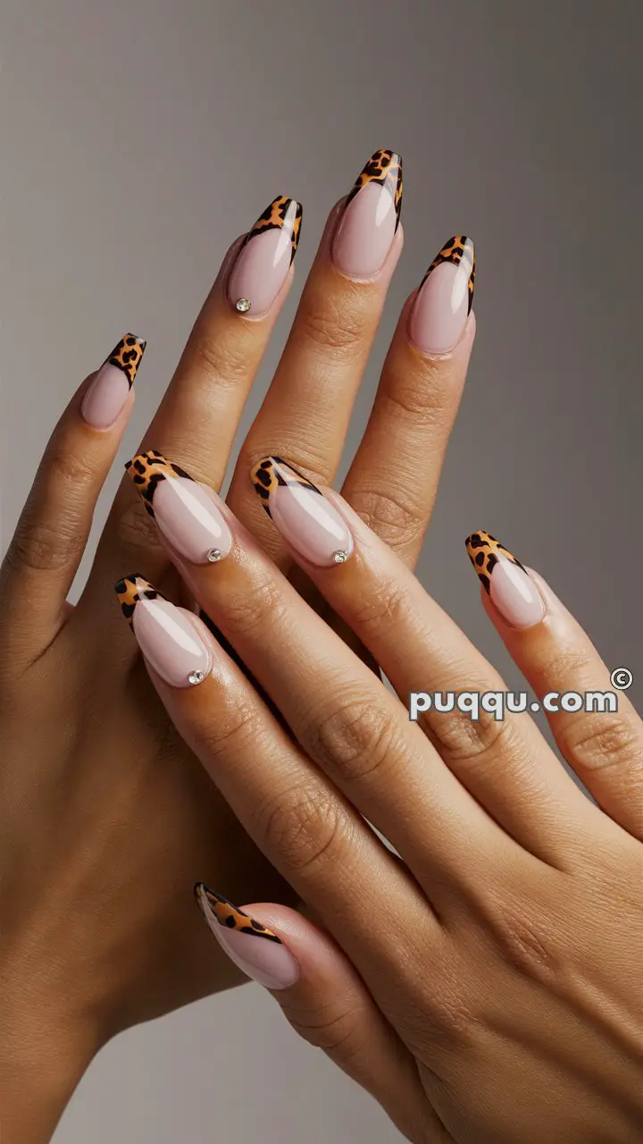 Hands with long nails featuring a leopard print French tip and sparkling rhinestone accents on a pale pink base.