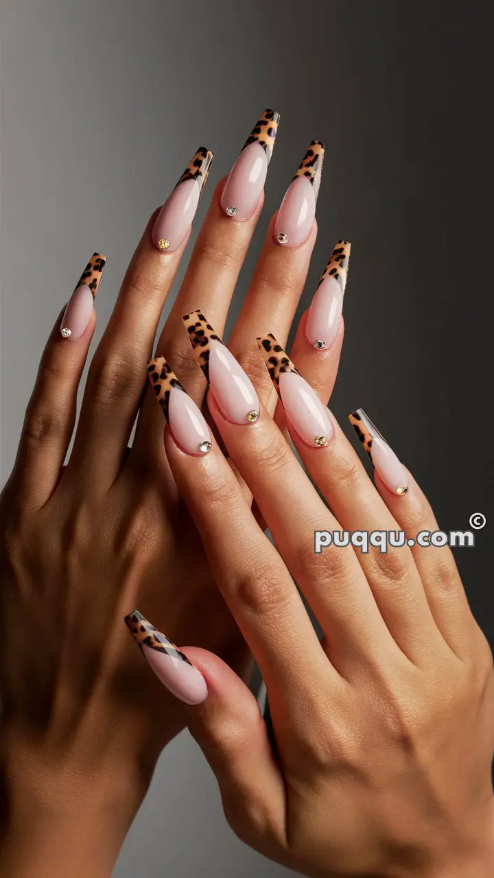 Hands with long, almond-shaped nails featuring a light pink base, leopard print tips, and small rhinestone accents near the cuticles.