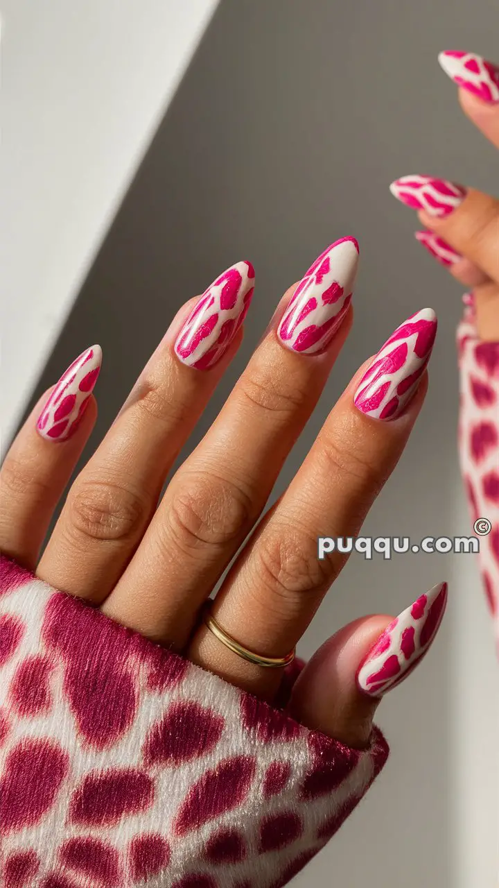 Close-up of a hand with long nails painted with a pink and white animal print design, wearing a pink patterned sleeve.