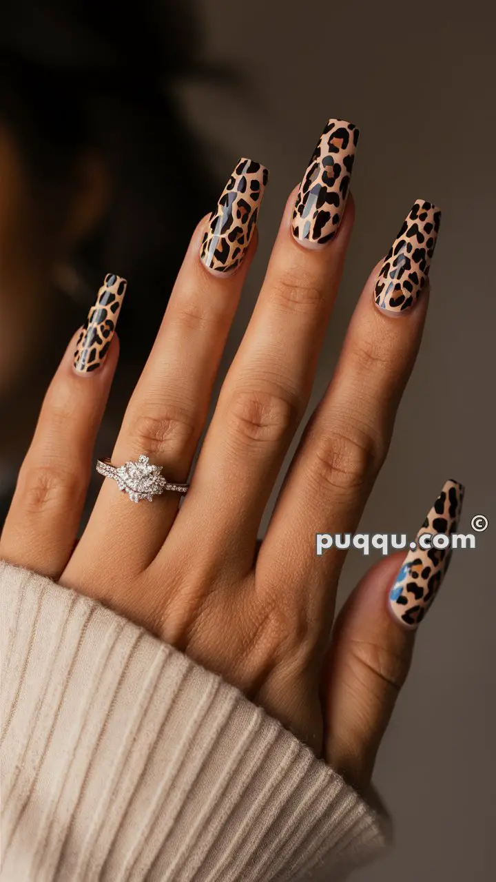 Hand with leopard print nail art and a diamond ring, wearing a beige ribbed sleeve.