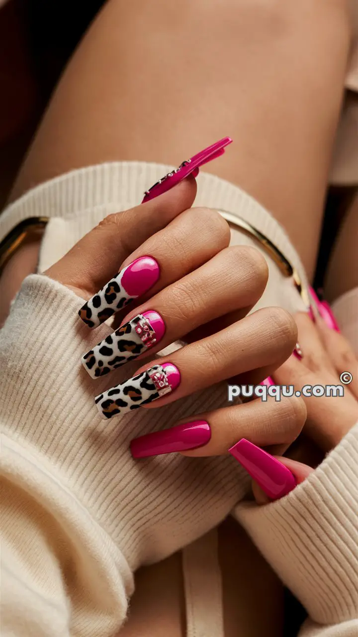 Hand with long, pink and leopard print acrylic nails with rhinestone accents.