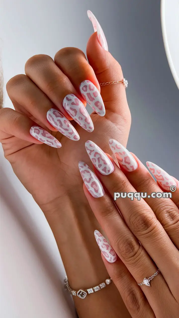 Hands with long, pointed nails featuring a white and pink animal print design, adorned with bracelets and rings.