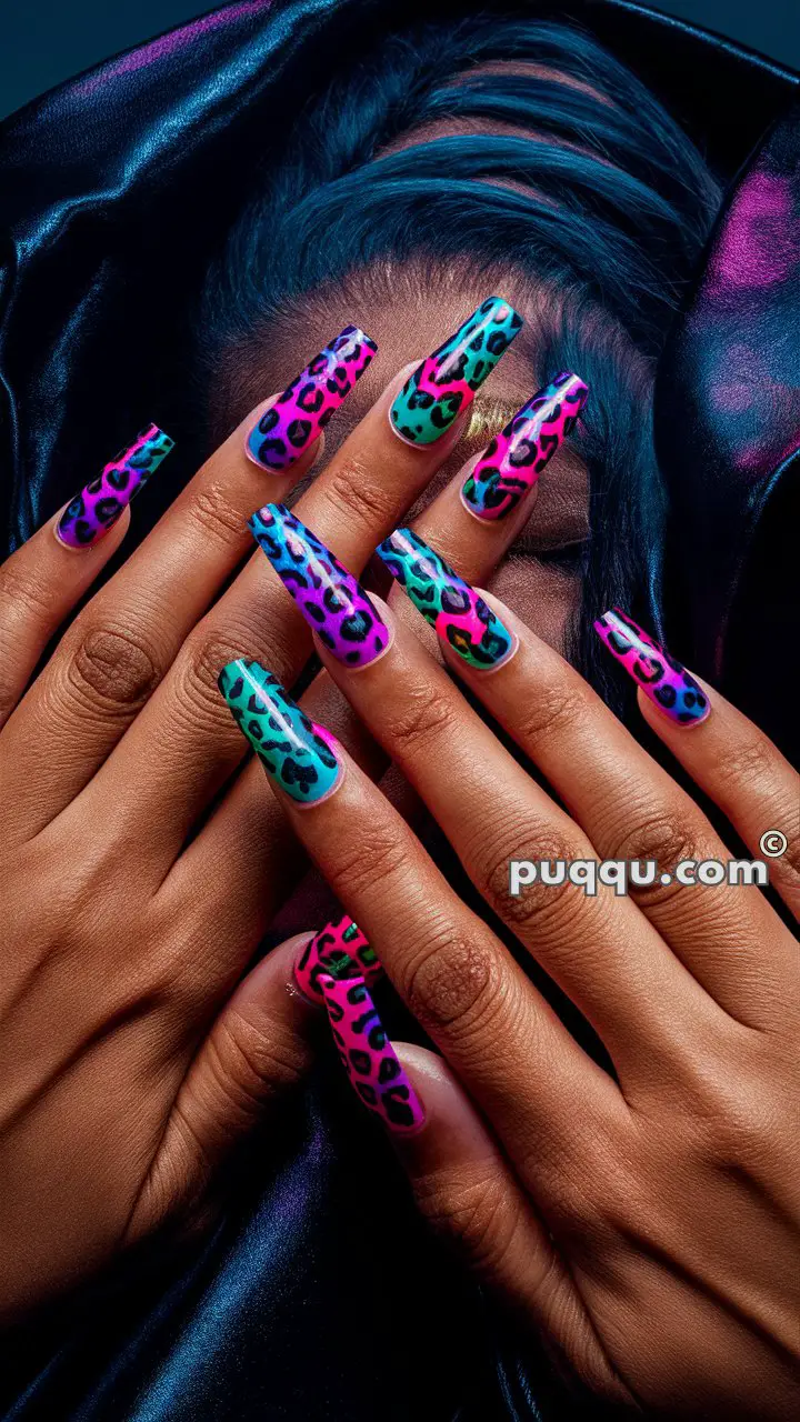 Hands with long, pointed nails featuring vibrant leopard print designs in blue, pink, purple, and green.