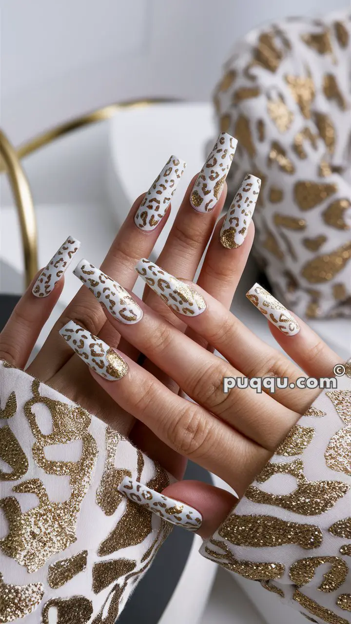 Hands with long, white nails featuring glittery gold leopard print design, matching the patterned sleeves.