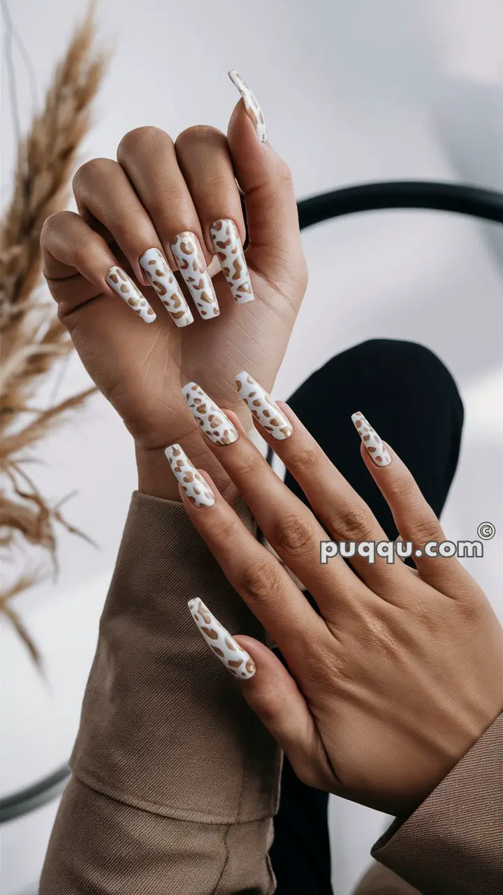 Hands with long, squared nails featuring a white base and brown abstract leopard print design.