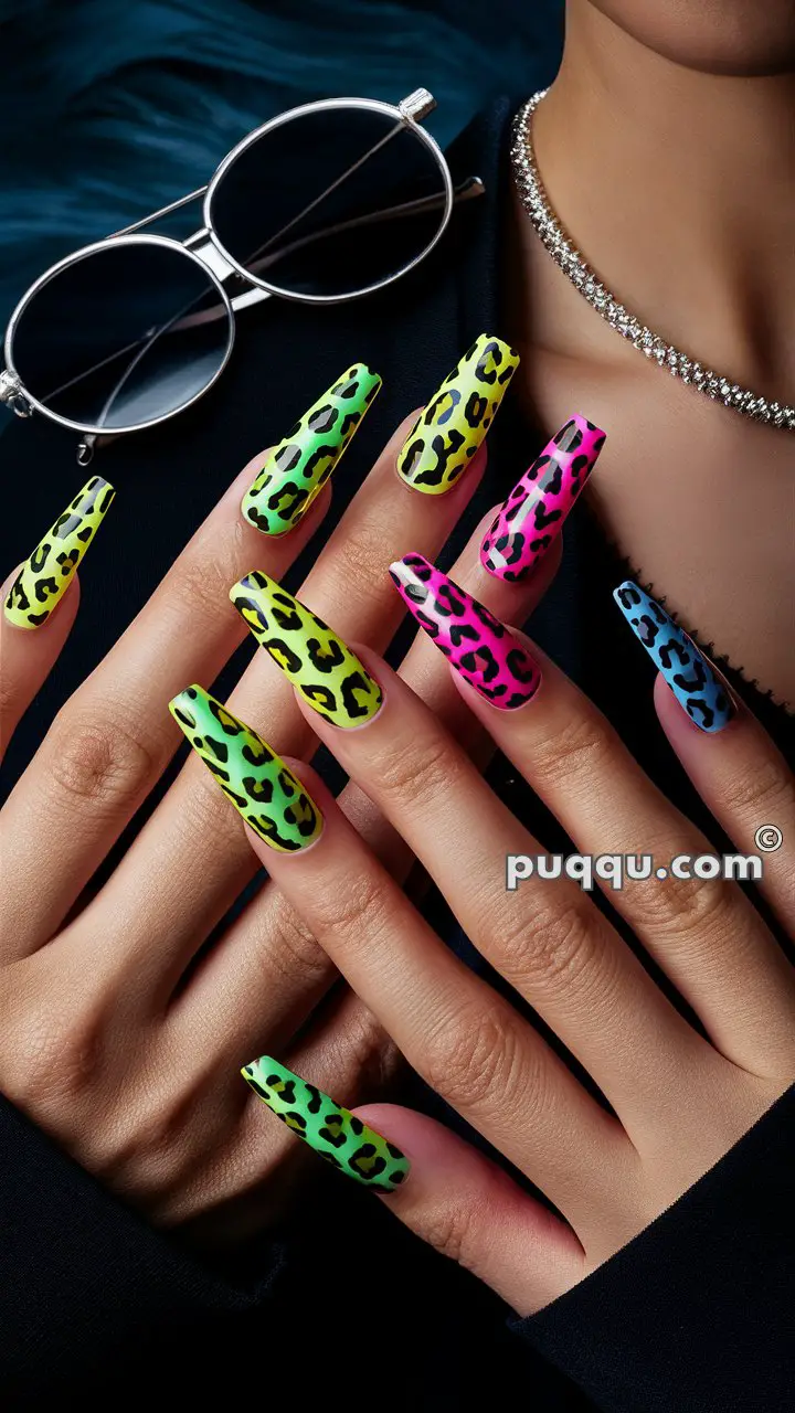 Hands showing off long, neon-colored leopard print nails in green, yellow, pink, and blue, with sunglasses and a sparkly necklace visible in the background.